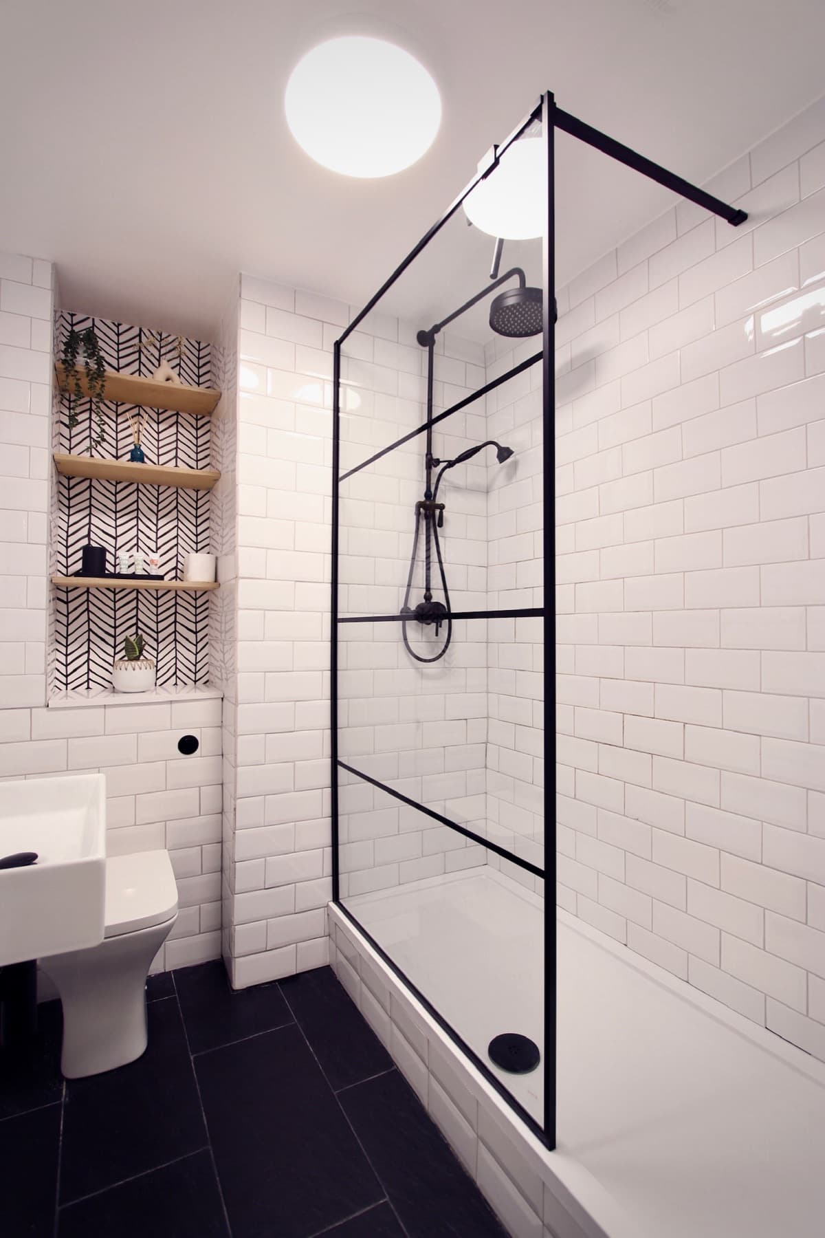 The walk-in shower behind a black-framed glass screen and white metro tiles